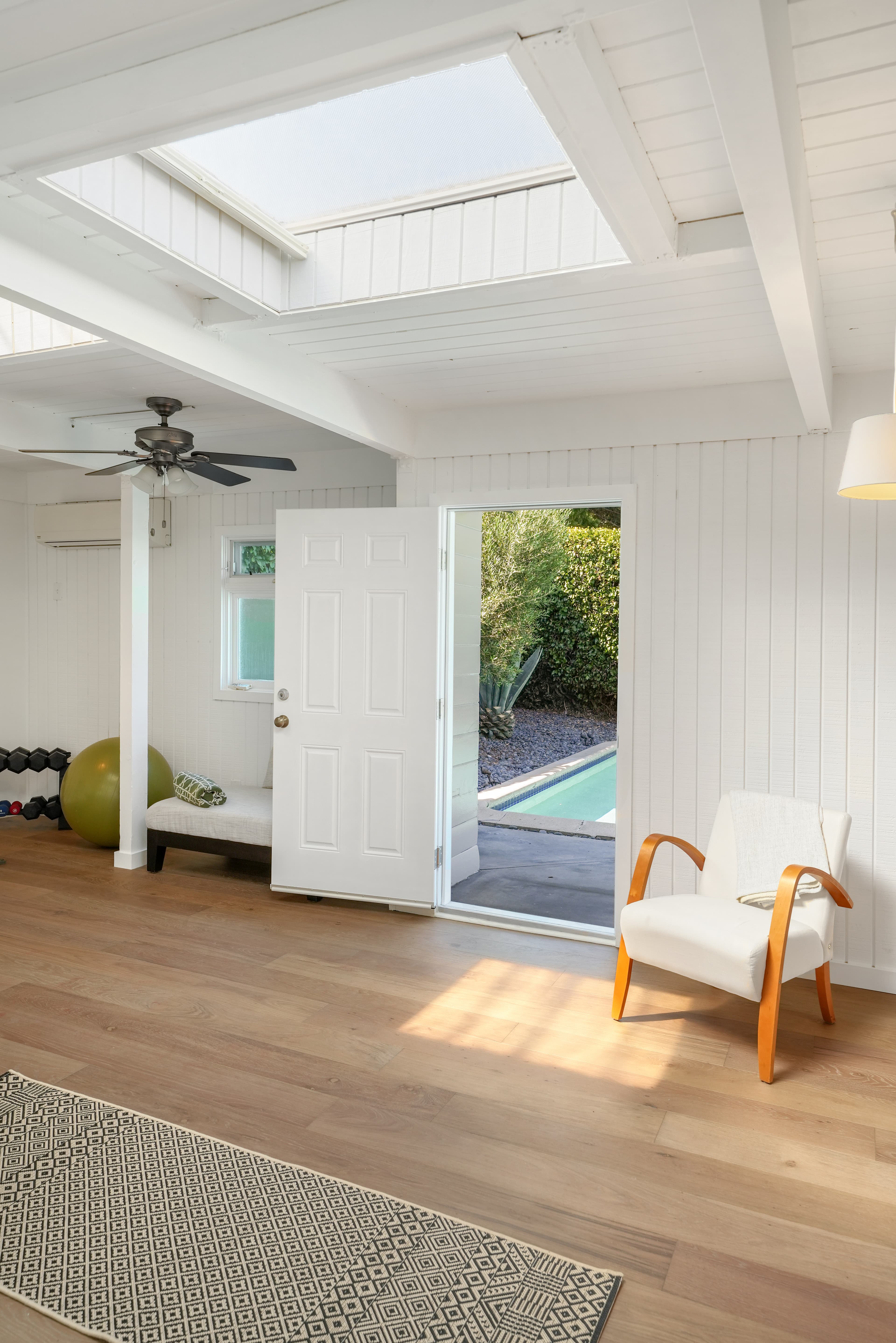 Sunlit white room with skylight, exercise equipment, and open door to a backyard pool.