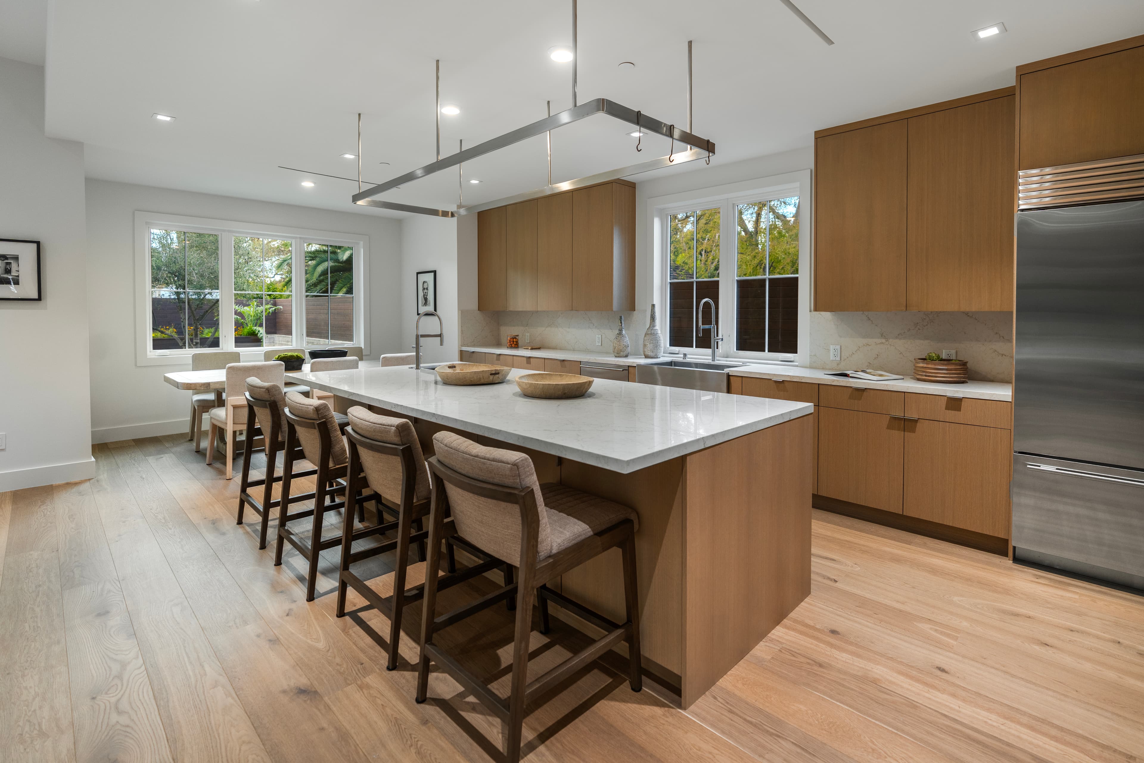 Modern kitchen featuring a large marble island, four bar stools, and light wood cabinetry.