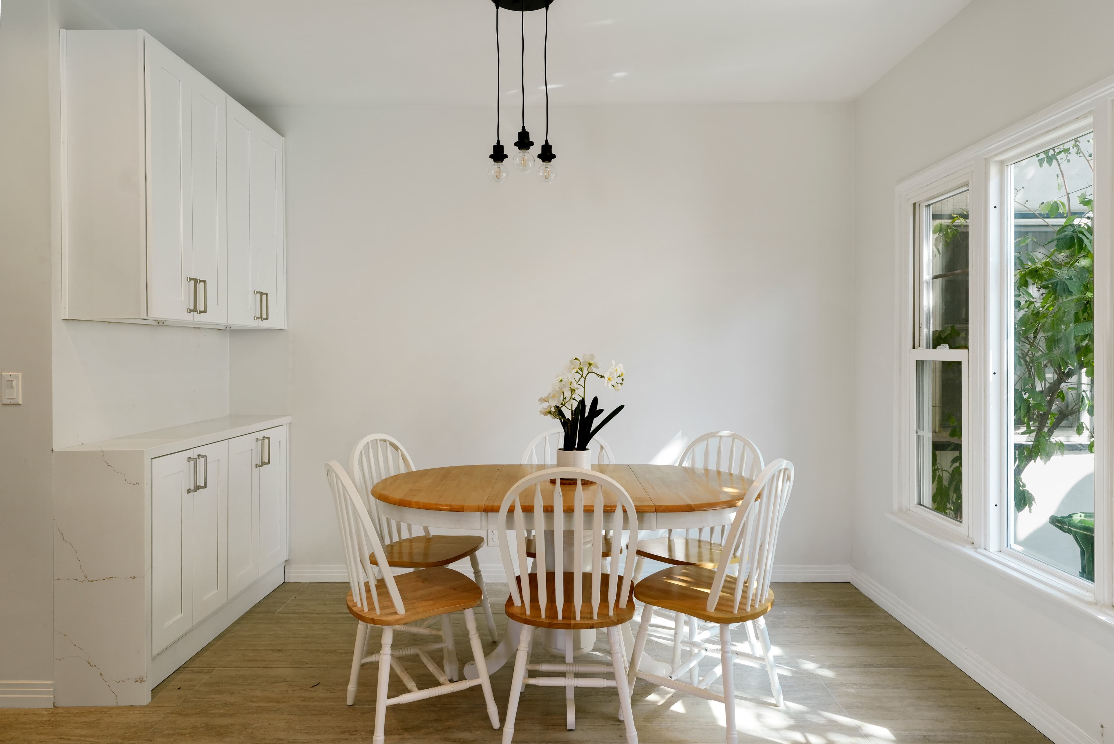 Bright dining room with a wooden table, white chairs, and minimalist white cabinetry.
