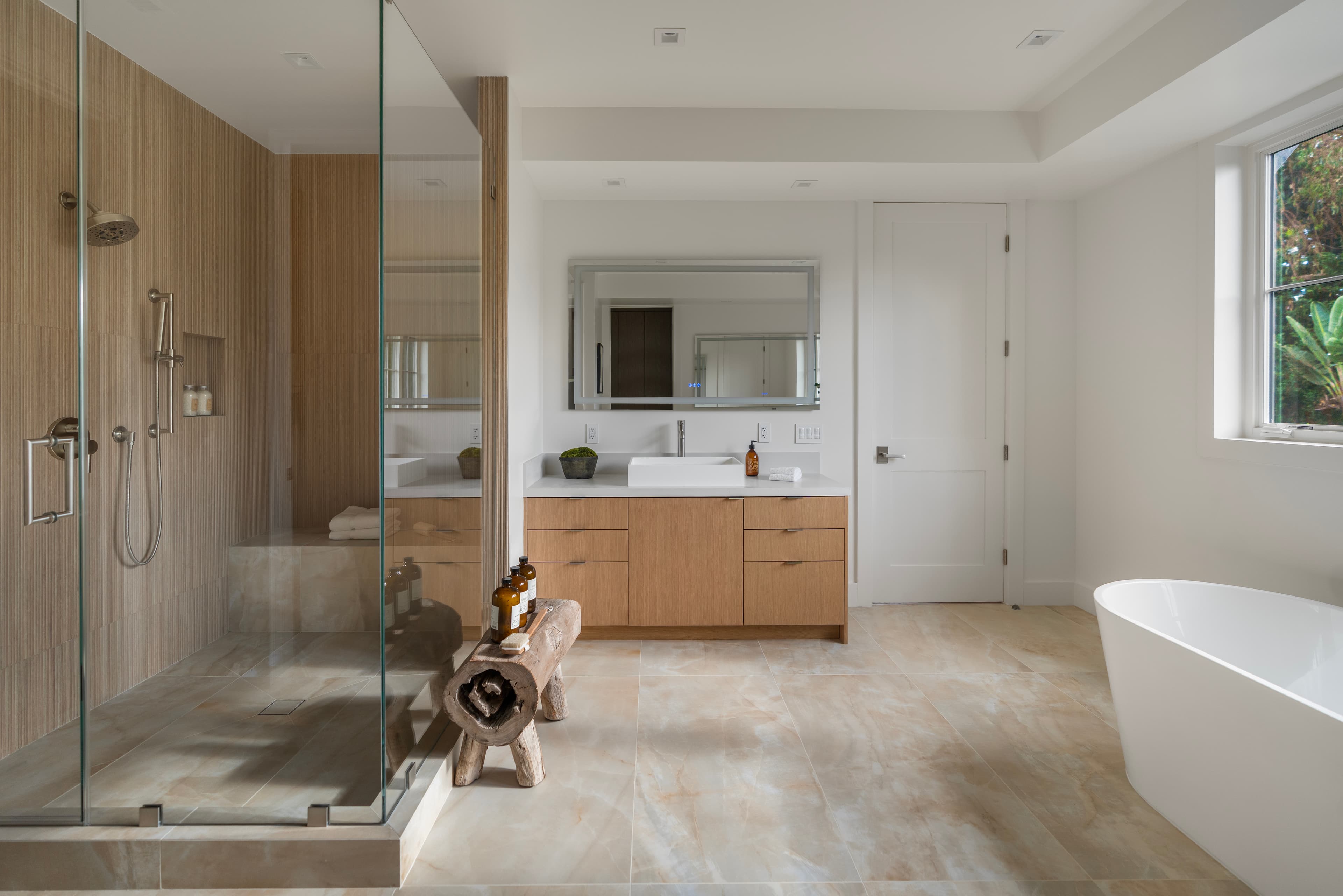 Modern bathroom featuring a glass walk-in shower, wooden vanity, and a freestanding white soaking tub.