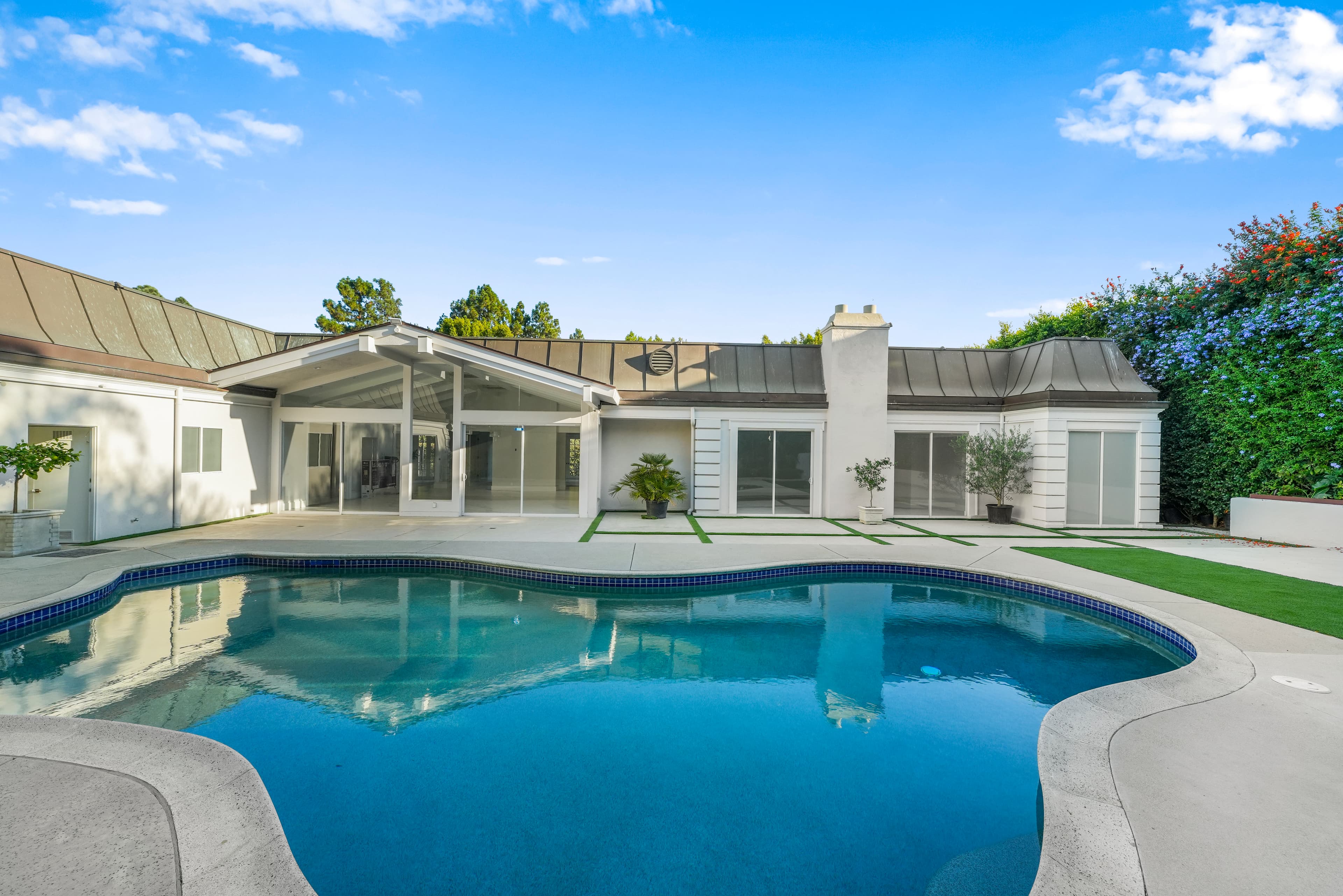 Modern white house with large glass windows and a curved swimming pool in the backyard.