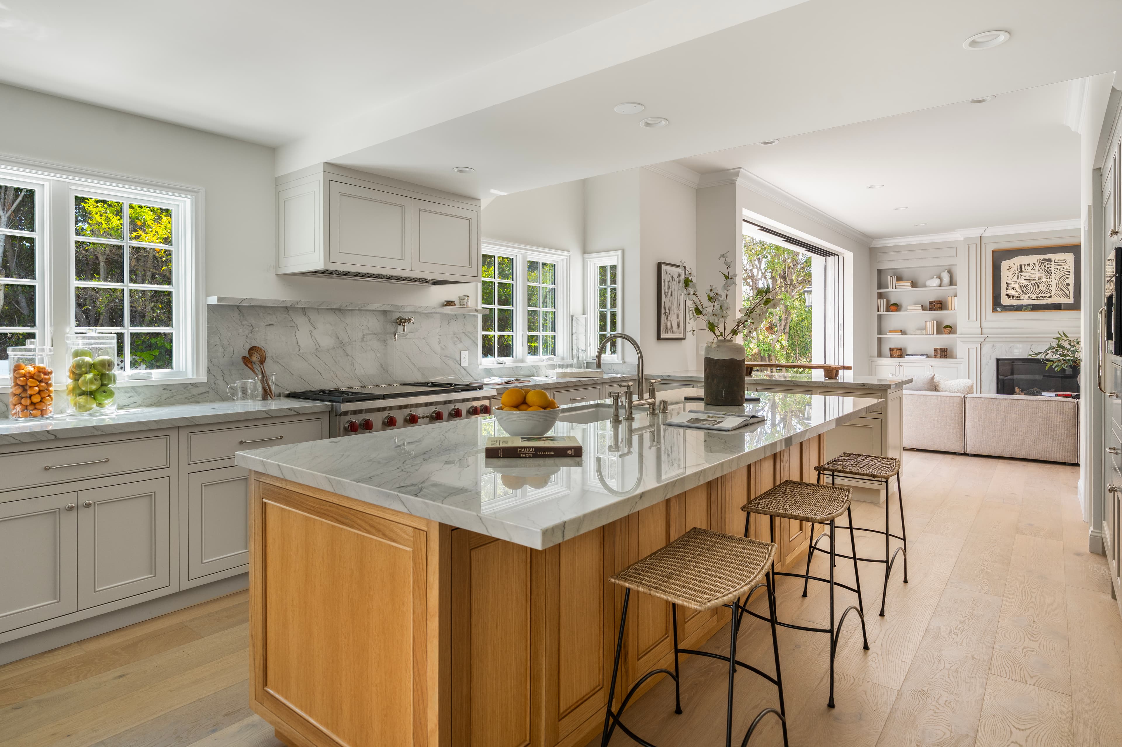 Modern kitchen with marble countertops, a wooden island with woven stools, and light grey cabinets.