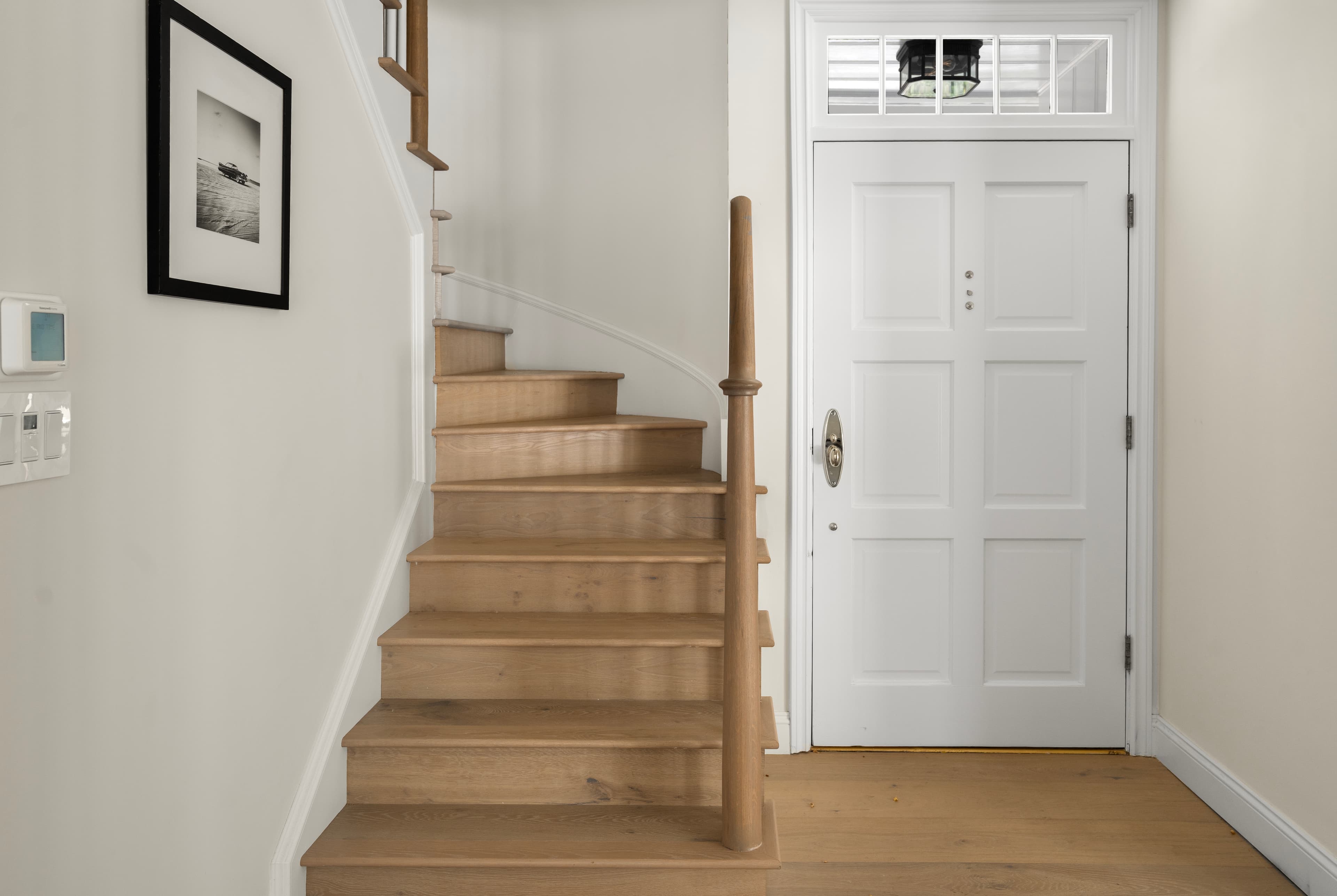 Bright home entryway featuring a light wood curved staircase beside a white paneled front door.