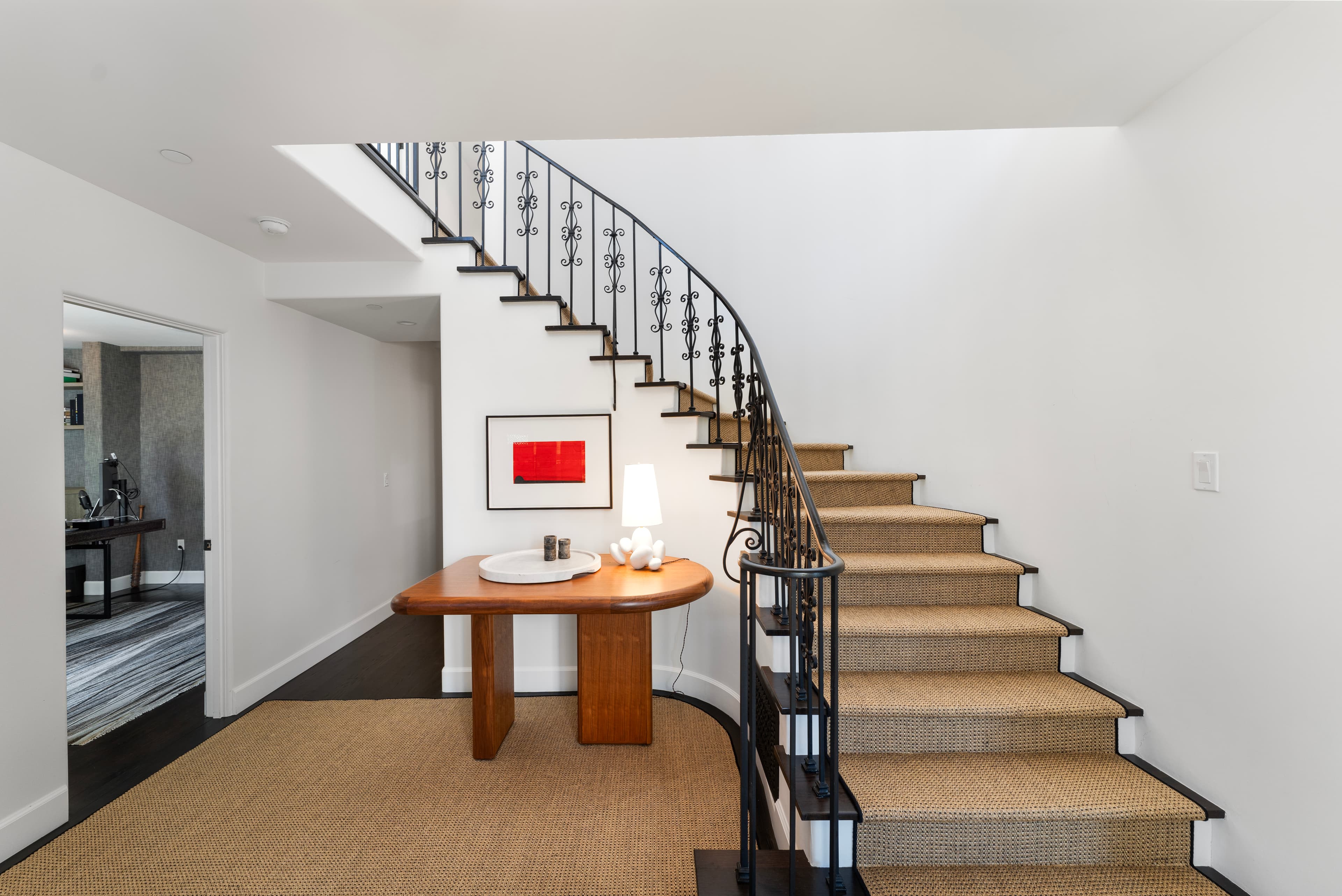 Curved staircase with black iron railing, tan carpet runners, and a wooden console table.