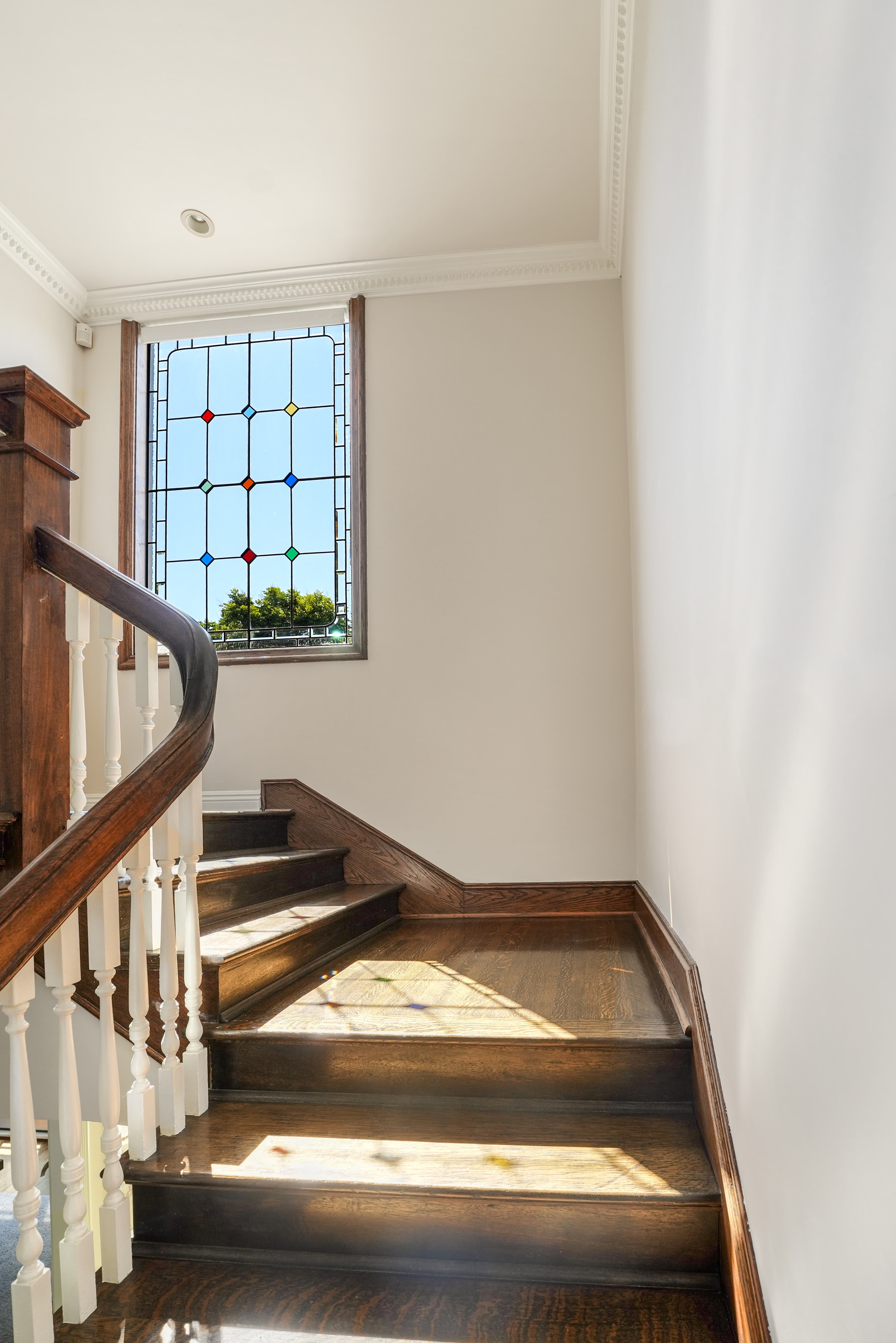 Sunlight streams through a stained glass window onto a dark wood staircase with white balusters.