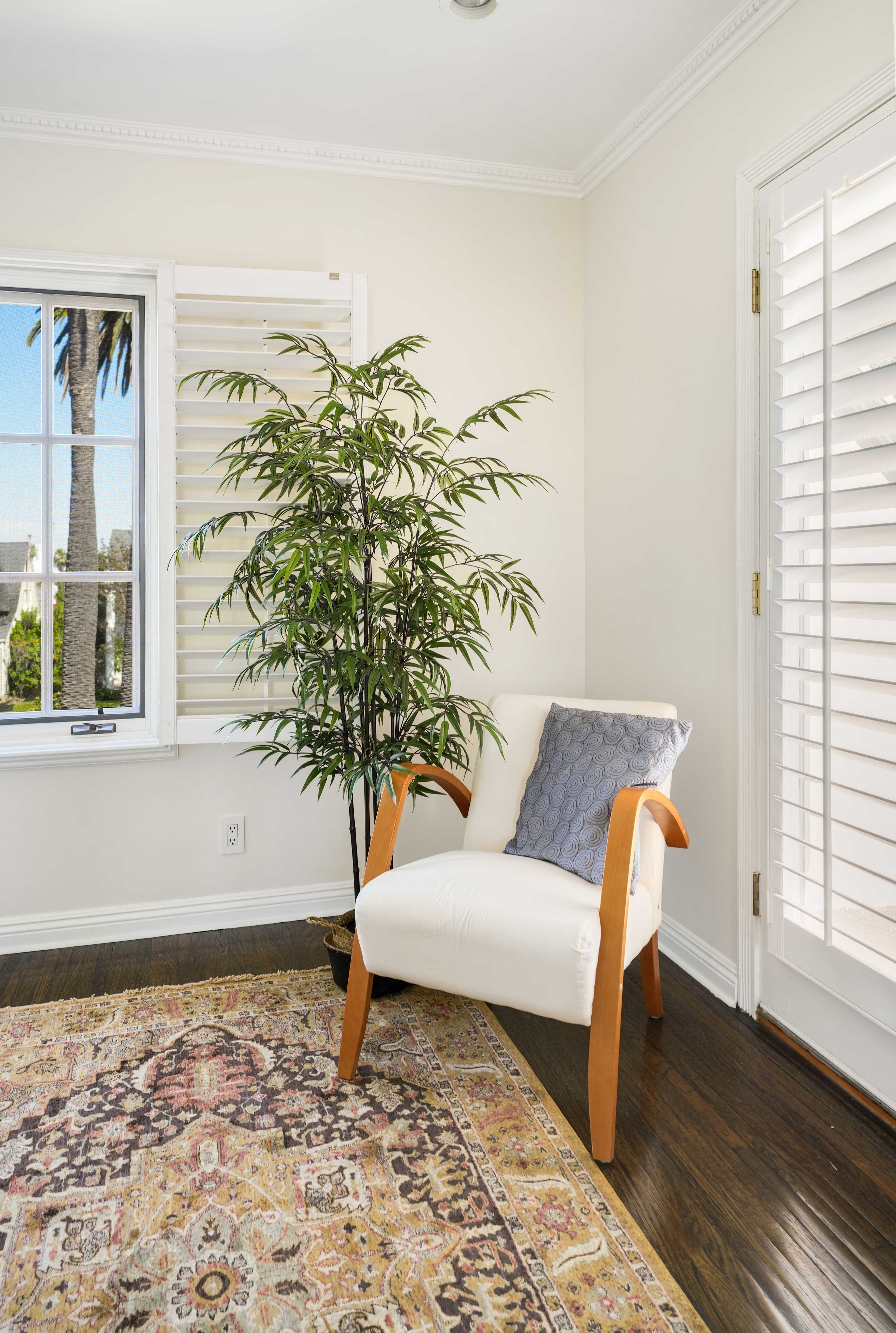 White armchair with blue pillow beside a tall green plant on a patterned rug.