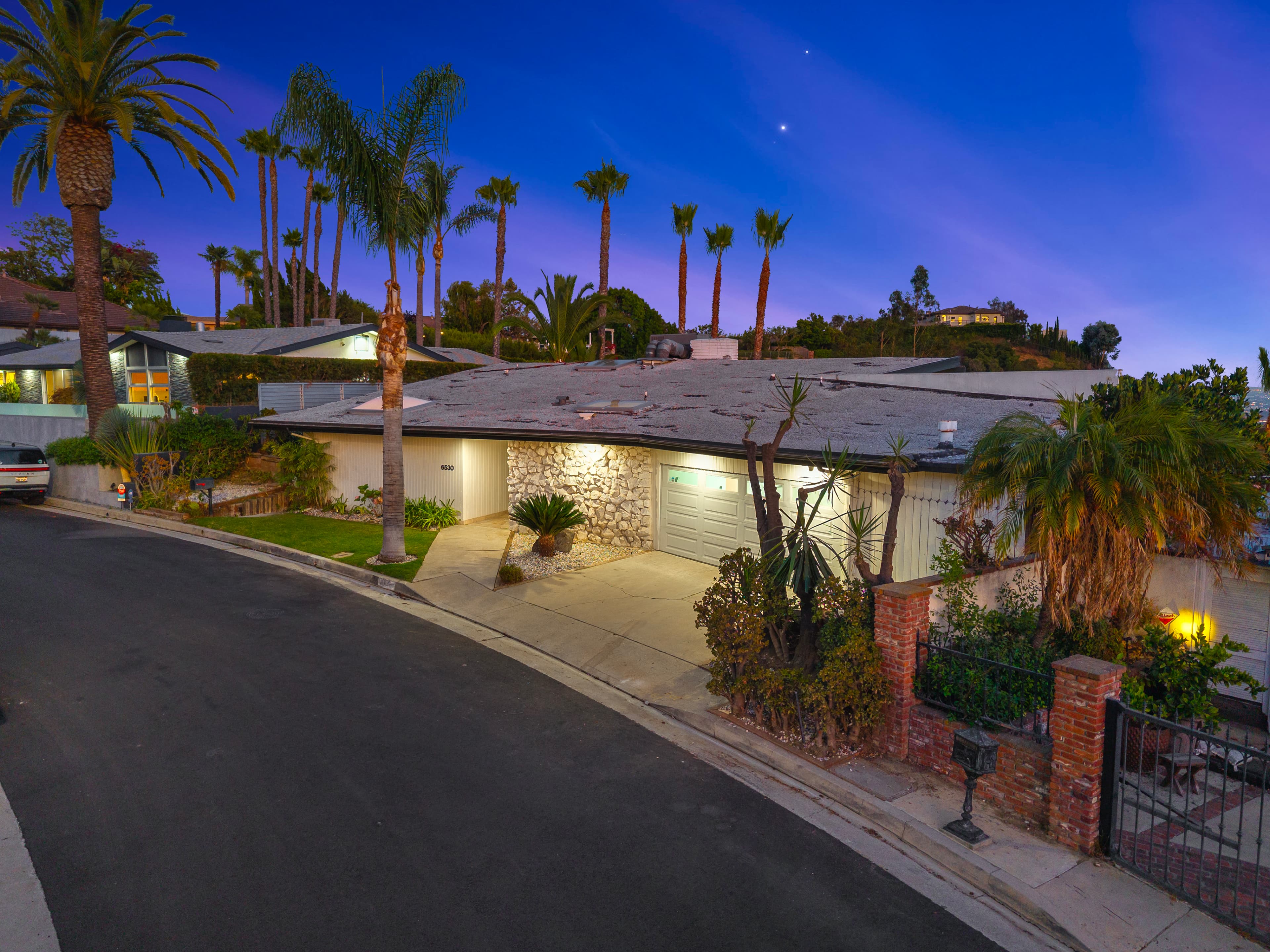 Modern ranch-style home with palm trees and stone accents under a colorful twilight sky.
